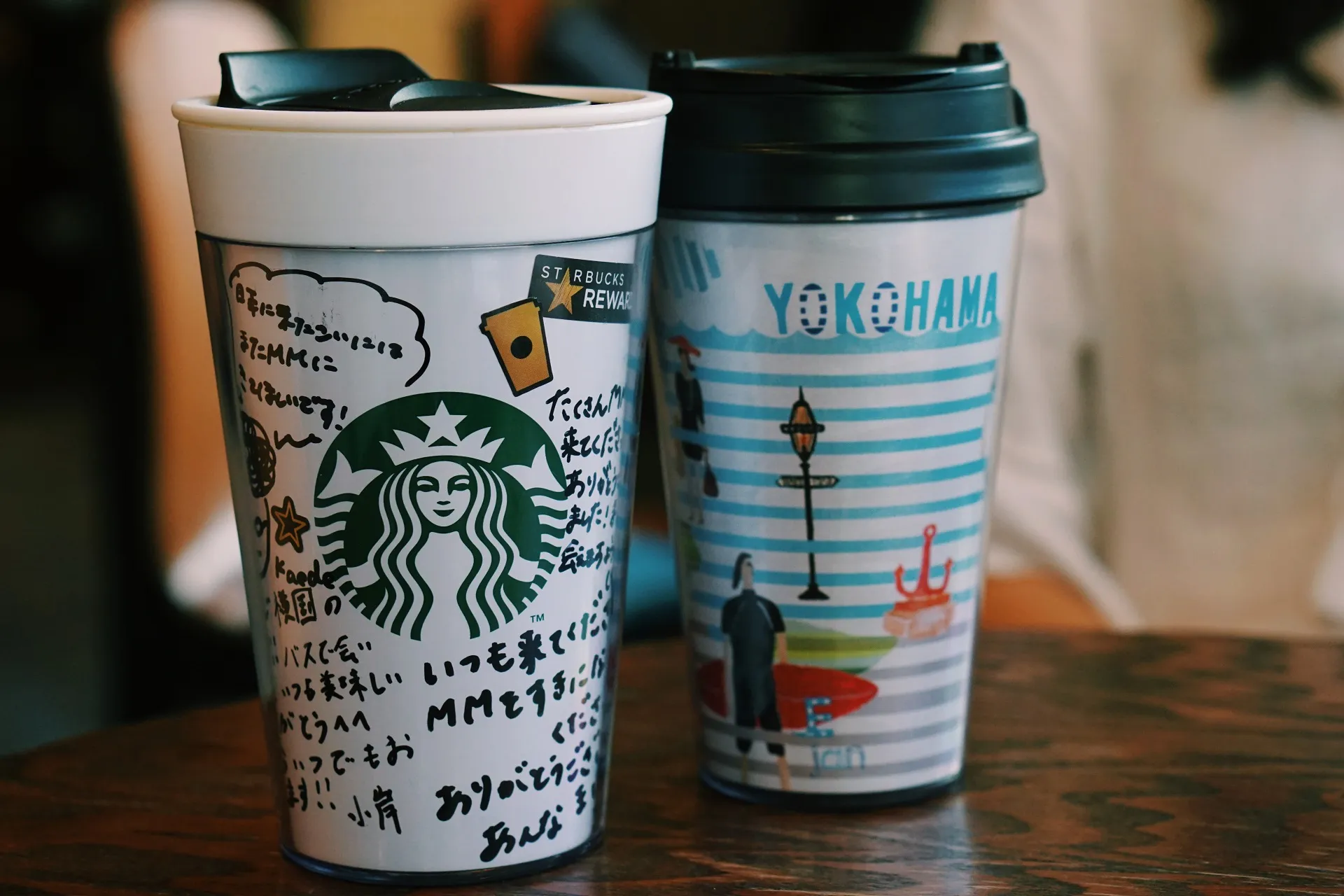 Chiếc cốc Starbucks MM21 với chữ ký, đặt cùng máy ảnh trên tủ sách